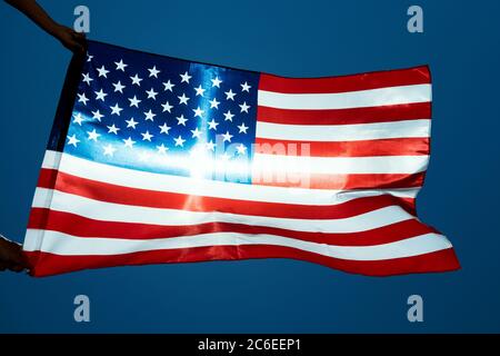 gros plan d'un homme portant un drapeau des États-Unis agitant sur le vent contre le ciel bleu, avec un sunbeam en arrière-plan Banque D'Images