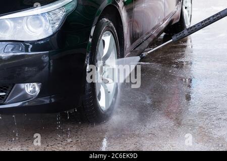 Nettoyage de la voiture noire avec de l'eau haute pression. Lavage manuel de voiture avec eau sous pression dans le lavage de voiture extérieur. Banque D'Images