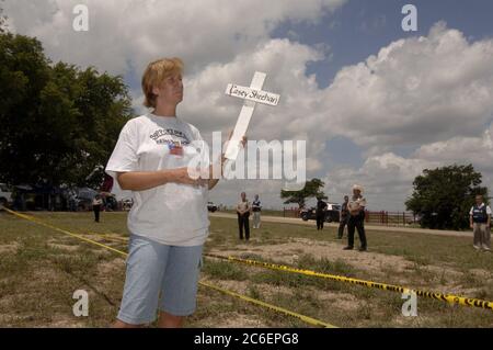 Crawford, Texas 12 août 2005 : la manifestante anti-guerre Cindy Sheehan, dont le fils Casey a été tué pendant la guerre d'Irak, tient une croix en bois blanche avec le nom de son fils dessus. Elle est sur le site de protestation connu sous le nom de 'Camp Casey' où environ 100 manifestants contre la guerre en Irak tiennent une veillée pendant les vacances du président américain George W. Bush en août dans son ranch voisin. Elle regarde le cortège du président passer alors qu'il partait pour une collecte de fonds. ©Bob Daemmrich Banque D'Images