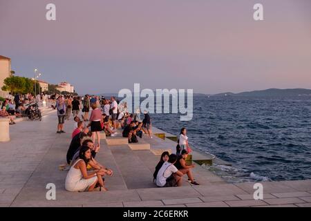 Les gens à l'orgue de mer au coucher du soleil, un monument public qui fait de la musique des vagues de mer, Zadar, Croatie Banque D'Images