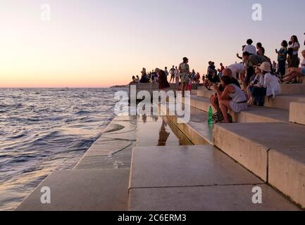 Les gens à l'orgue de mer au coucher du soleil, un monument public qui fait de la musique des vagues de mer, Zadar, Croatie Banque D'Images