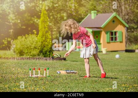 Mignon 6 ans enfant fille jouer corde broche jeu de lancer dans le jardin à la maison dehors le jour ensoleillé d'été. Concept d'activité de loisirs. Banque D'Images