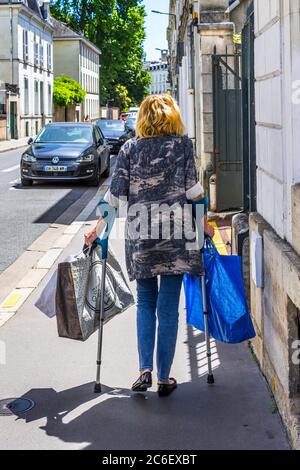 Femme dans ses années 50 portant des sacs d'achats et utilisant des aides à la marche - Tours, France. Banque D'Images