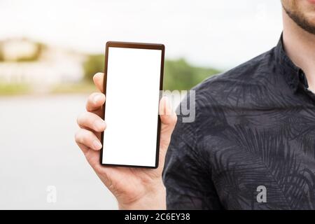 Image de la main de homme tenant le téléphone portable noir moderne avec écran blanc vierge. Homme utilisant un smartphone mobile, gros plan. Banque D'Images