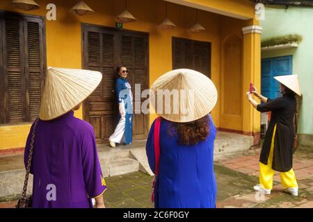 Un groupe de femmes asiatiques en chapeaux vietnamiens Prenez une photo d'un ami à l'extérieur d'une maison jaune Banque D'Images
