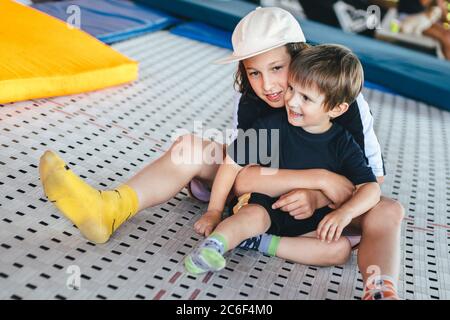 Drôle de sourire enfants sur trampoline. Le frère aîné embrasse plus jeune. Repos actif dans le centre sportif. Deux heureux émotions garçons, frères jouant et Banque D'Images