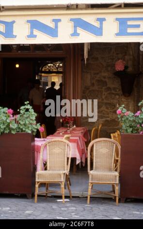 Chaises tissées traditionnelles à côté de jardinières pleines de plantes pélargonium roses et tables posées pour les dîners sous une verrière à l'extérieur d'un restaurant sur la place du marché à St Cast le Guildo, Bretagne, France 1984. Banque D'Images