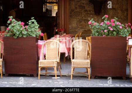 Chaises tissées traditionnelles à côté de jardinières pleines de plantes pélargonium roses et tables posées pour les dîners sous une verrière à l'extérieur d'un restaurant sur la place du marché à St Cast le Guildo, Bretagne, France 1984. Banque D'Images