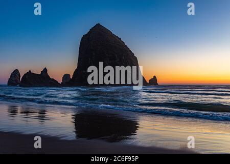 Les oiseaux survolent Haystack Rock et les piles de la mer au coucher du soleil le long de Cannon Beach, en Oregon Banque D'Images