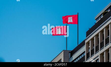 deux drapeaux rouges de la ville hanséatique de hambourg avec blason agite dans le vent sur un immeuble de bureaux. photographie horizontale Banque D'Images