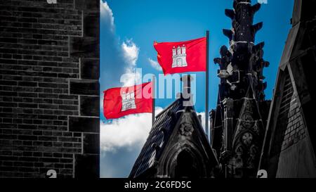 deux drapeaux rouges de la ville hanséatique de hambourg avec des armoiries agitant dans le vent sur le mémorial st. nikolai. photographie horizontale Banque D'Images