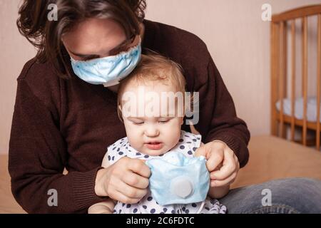 L'enfant ne veut pas porter de masque médical. Une fille d'un an sur fond beige prend un respirateur bleu. Espace vide pour le texte. L'enfant p Banque D'Images