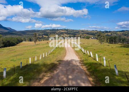 Vue aérienne d'une route en terre avec des marqueurs blancs de poste de clôture dans un champ agricole vert Banque D'Images