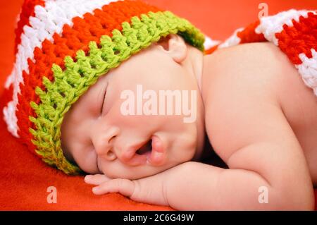 Magnifique nouveau-né bébé garçon avec un joli chapeau dormant paisiblement sur la couverture rouge doux Banque D'Images