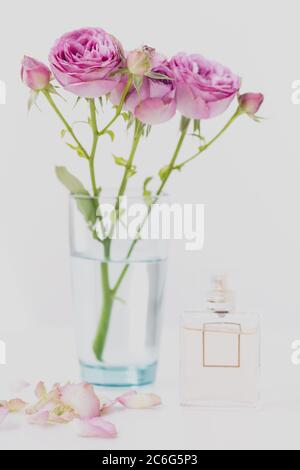 Fleurs roses - roses dans un vase, à côté d'une bouteille avec parfum sur un fond flou. Banque D'Images