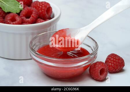 Sauce à la framboise, confiture de framboise dans un bol en verre avec cuillère, framboises, Allemagne Banque D'Images