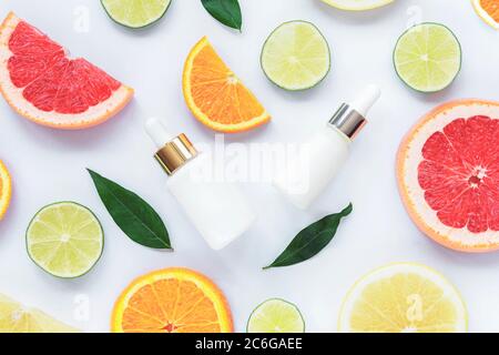 Flacons compte-gouttes blancs avec sérum cosmétique et agrumes en tranches. Cosmétiques naturels avec vitamine C. vue du dessus, plat. Banque D'Images