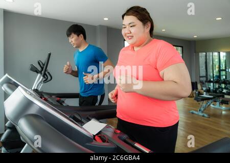 Deux formateurs de l'Asie et de l'embonpoint homme femme l'exercice de formation sur tapis roulant dans une salle de sport, formateur thump vers elle pour bon résultat lors de l'entraînement. Grosses Femmes Banque D'Images