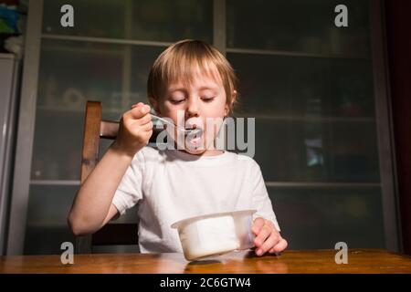 Adorable petite fille mangeant du fromage cottage de la cuillère, en-cas de lait sain. Banque D'Images