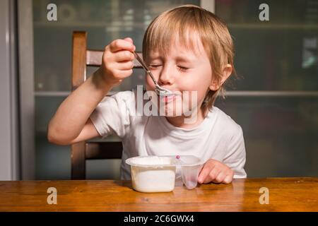 Adorable petite fille mangeant du fromage cottage de la cuillère, en-cas de lait sain. Banque D'Images