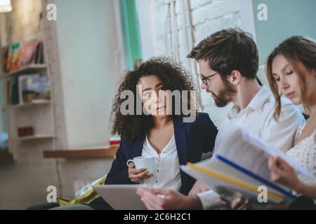 Fille avec tasse et gars avec ordinateur portable parlant petite amie avec dossiers Banque D'Images