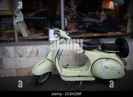 Photographie de rue.Un couple de jeunes hommes lisant à l'intérieur d'une librairie en tant que mobylette vert menthe clair se trouve à l'extérieur, attendant son propriétaire, à Sydney, Nouvelle-Galles du Sud, Australie Banque D'Images