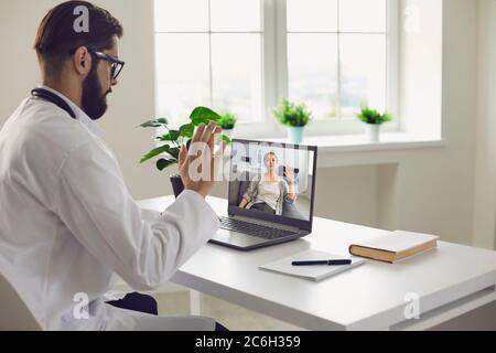 Consultation médicale à distance. Un médecin de sexe masculin consulte une femme dispose d'un moniteur d'ordinateur de vidéoconférence installé dans un bureau de clinique. Banque D'Images