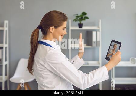 Médecin en ligne. Une femme médecin accueille le patient avec une tablette d'appel avec caméra vidéo dans le bureau de la clinique. Banque D'Images