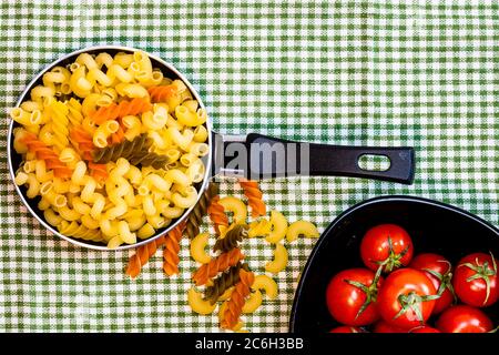 Petite petite poêle à frire avec pâtes fusilli crues tricolores dans une composition rustique. Banque D'Images