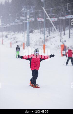 Un homme heureux en veste rouge sur le ski de snowboard en montagne. Il neige Banque D'Images