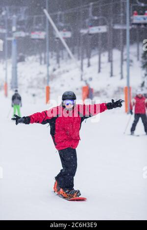 Un homme heureux en veste rouge sur le ski de snowboard en montagne. Il neige Banque D'Images