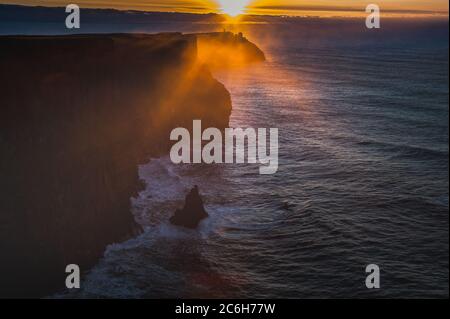 Le soleil se couche sur les falaises de Moher tandis que la brume s'élève de l'océan Atlantique. Coucher de soleil brumeux ou brumeux sur des falaises spectaculaires tandis que les rayons du soleil se précipitent dans la brume Banque D'Images