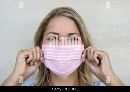 Jeune femme portant un masque rose portrait - Blonde femelle utilisant un masque facial protecteur pour prévenir la propagation du virus corona Banque D'Images