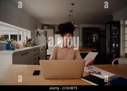 Femme d'affaires sérieuse et ciblée qui tape sur des papiers de conservation pour ordinateur portable pour préparer un rapport d'analyse des résultats de travail Banque D'Images