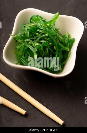 Sélection sélective, salade de Chuka de mer aux graines de sésame dans des plats en céramique blanche, avec des bâtonnets de bambou sur fond sombre Banque D'Images