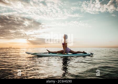 Jeune femme faisant DU YOGA sur un panneau SUP dans le lac au lever du soleil Banque D'Images