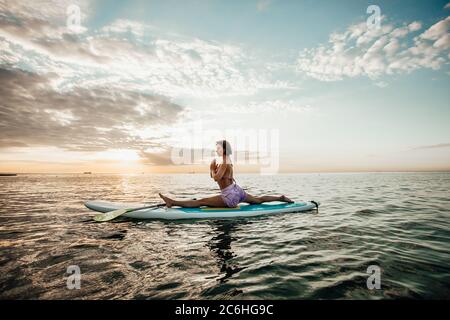 Jeune femme faisant DU YOGA sur un panneau SUP dans le lac au lever du soleil Banque D'Images