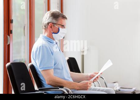 Homme mature dans une salle d'attente lumineuse d'un hôpital lisant le résultat du test de Covid-19 Banque D'Images