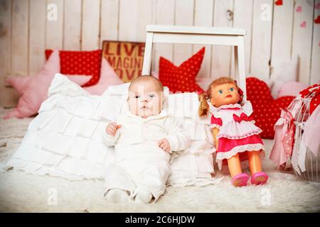 Bébé garçon dans un costume blanc élégant est assis à côté d'une poupée vintage dans une robe rose. Banque D'Images