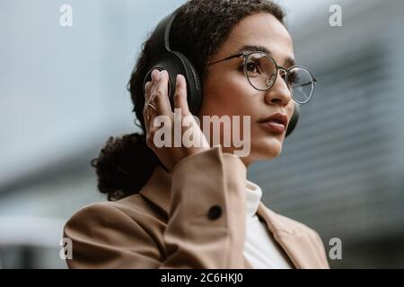 Femme d'affaires utilisant un casque sans fil lors de ses déplacements au travail. Femme de direction écoutant de la musique avec un casque. Banque D'Images