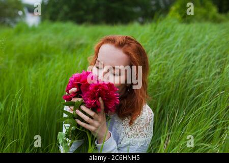 La fille REDHEAD sent le bouquet de pivoines dans le champ Banque D'Images