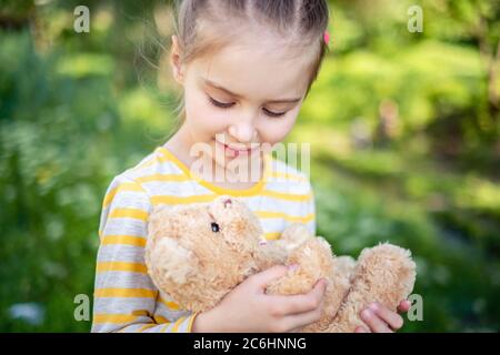 Petite fille adorable avec son jouet ours en peluche préféré au parc en été Banque D'Images