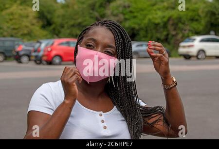 Angleterre, Royaume-Uni. 2020. Portrait d'une femme noire avec un style de cheveux tressé ajustant son masque de couleur rose pendant l'épidémie de Covid-19 Banque D'Images