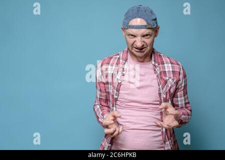 Homme en colère dans une casquette et des vêtements décontractés regarde furfurieusement et fait un geste avec ses mains. Copier l'espace. Banque D'Images