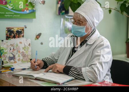 Une infirmière âgée prescrit une ordonnance médicale pour le patient. La femme âgée masquée écrit sur la carte du patient. Hôpital de la ville. Mai 2020, Brovary, Ukraine Banque D'Images