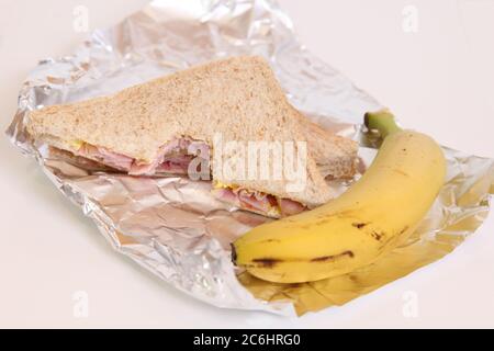 Demi-sandwich au jambon mangé avec banane, panier repas dans du papier d'aluminium sur blanc Banque D'Images