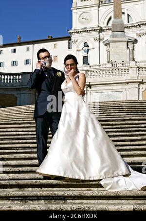 Couple nouvellement marié portant un masque médical coronavirus, posant pour prendre des photos sur les marches espagnoles. Mariage au temps de Covid 19 Rome Italie Europe Banque D'Images