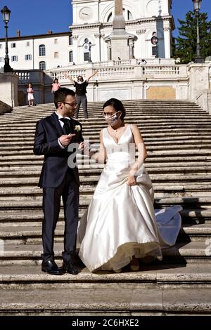 Couple nouvellement marié portant un masque médical coronavirus, posant pour prendre des photos sur les marches espagnoles. Mariage au temps de Covid 19 Rome Italie Europe Banque D'Images