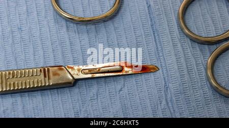 Lame de scalpel chirurgicale recouverte de sang, sur un plateau à côté d'autres instruments chirurgicaux Banque D'Images