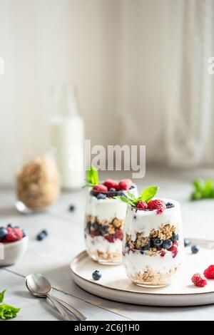 Deux verres de parfait en granola, baies et yaourt sur la table. Prise de vue en angle avec placement pour le texte, mise au point sélective. Banque D'Images